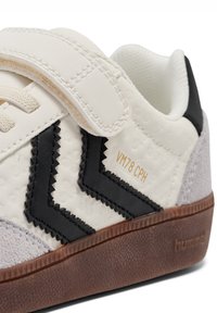 Weißer Ledersneaker mit schwarzen Zickzack-Akzenten, grauem Wildlederabsatz, Klettverschluss und einer strukturierten braunen Gummisohle. Mit der Aufschrift "VM78 CPH" in Gold.