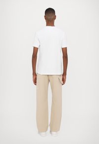 Hvit bomull t-skjorte, rund hals, korte ermer, kombinert med beige cargo bukser, vide ben, to lommer, enkelt design, brukt med hvite sko.