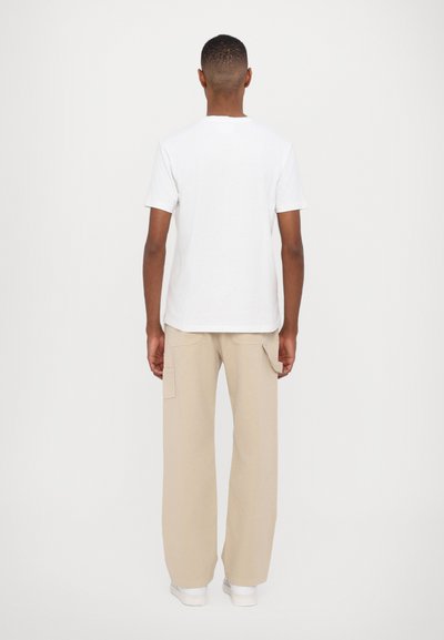 Hvid bomulds T-shirt, rund halsudskæring, korte ærmer, parret med beige cargobukser, bred ben, to lommer, enkelt design, båret med hvide sko.