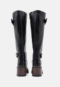 Bottes noires en cuir à hauteur de genoux avec un design structuré, dotées d'une fermeture éclair à l'arrière, de détails en sangle croisée et d'un talon en bois brun.