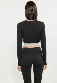 Zwarte lange mouwen crop top met een contrasterende grijze band aan de onderkant, gecombineerd met zwarte high-waisted legging. Zachte, rekbare stof.