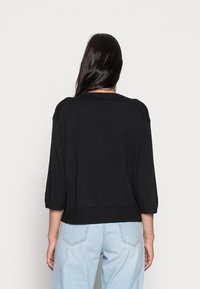 Pull en tricot noir à manches trois-quarts, col rond et ourlet côtelé. Porté avec un jean en denim bleu clair.