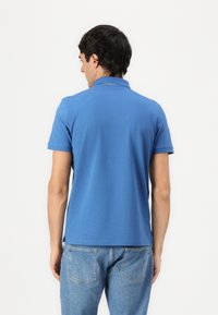 Blå polo t-shirt lavet af bomuld med krave og korte ærmer. Har en lige pasform og sideslidser i kanten. Bæres med lyseblå jeans.