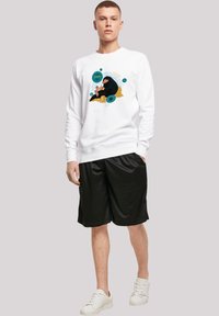 Hvit, langermet genser med en fargerik grafisk design på forsiden. Kombinert med svarte shorts og hvite joggesko.
