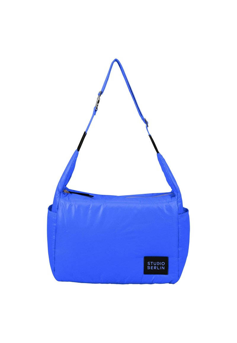 Borsa a tracolla blu con imbottitura, tracolla regolabile, chiusura superiore con cerniera e tasca laterale. Presenta un'etichetta nera con il logo "STUDIO BERLIN."