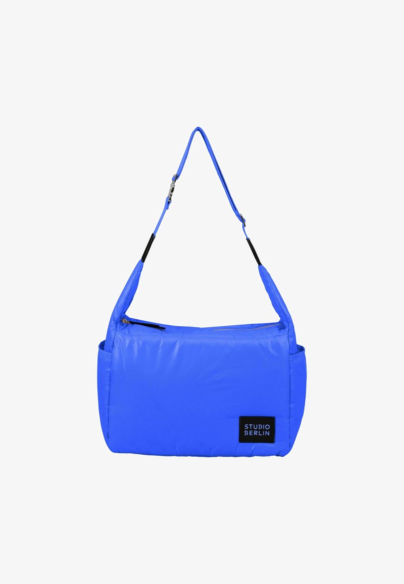 Modrá polstrovaná kabelka s nastavitelným popruhem, zipovým uzavřením nahoře a boční kapsou. Obsahuje černou nášivku s logem označenou "STUDIO BERLIN."