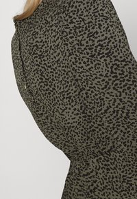 Vêtement vert avec un motif tacheté noir de léopard. Présente un col arrondi et une taille froncée, fabriqué à partir d'un tissu doux et texturé.