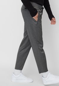 Grå smalnade byxor med dragsko i midjan, sidofickor och en subtil textur, parat med vita sneakers och en ribbad svart topp.