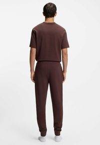 Weinrotes, strukturiertes Kurzarmoberteil kombiniert mit passenden Hosen. Beide haben eine lockere Passform und einen elastischen Bund, gezeigt von hinten.