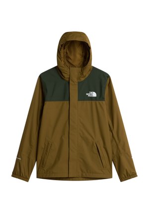 Jongen draagt een bruin-groene jas, grijze muts, grijze trui, zwarte broek en zwarte schoenen, staat met handen in de zakken en sleutels bevestigd aan de broek.