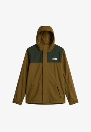 Dreng iført en brun-grøn jakke, grå hue, grå sweatshirt, sorte bukser og sorte sko, står med hænderne i lommerne og nøgler fastgjort til bukserne.