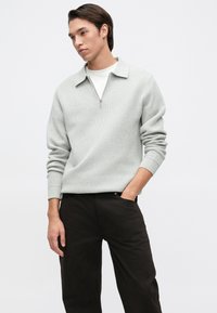 Pullover cinza claro com fecho de zíper de um quarto, punhos canelados e colarinho descontraído, combinado com calças pretas, com uma textura suave e ajuste solto.