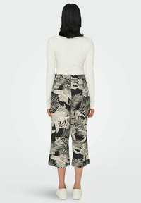 Wide-leg trousers with a black base featuring a white tropical leaf and floral pattern. Paired with a long-sleeve white top and white shoes.