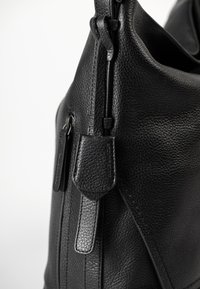 Schwarze, genarbte Lederhandtasche mit sichtbarem Reißverschluss und Lederstrapazierdetails auf einem schlichten weißen Hintergrund.