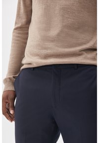 Beige stickad tröja och marinblå byxor. Tröjan har en texturerad yta, medan byxorna har platt front och en slank design.