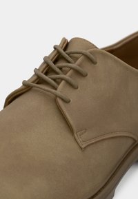 Close-up of a tan suede dress shoe with round laces and visible stitching on the side and tongue.