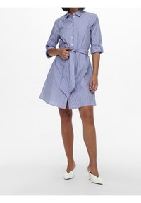 Abito a camicia a righe blu e bianche, con colletto, chiusura a bottoni e cintura in vita. Le maniche sono arrotolate e il design è lungo fino al ginocchio.