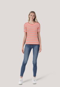 Rot-weiß gestreifes T-Shirt mit kurzen Ärmeln und rundem Halsauschnitt, kombiniert mit blauen Skinny-Jeans und weißen Sneakers.