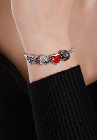 Zilveren charmearmband met hartvormige charms. Een charm is van rood emaille, een andere heeft gegraveerde tekst, met een bloemmotief en heldere stenen.
