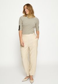 Triibuline, keha järgnev beež kaelusega pusa mustade triipudega, kombineeritud lõdvestunud beežide pükstega. Käised on küünarnukini ning neil on dekoratiivsed nupud.