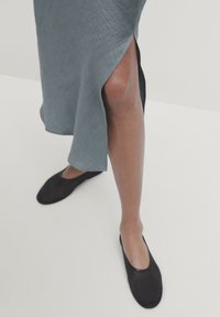 Robe bleu clair à mi-longueur avec une fente latérale, faite d'un tissu texturé. Portée avec des ballerines noires minimalistes.