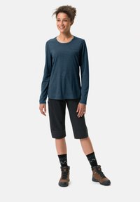 Mørkeblå langermet topp kombinert med svarte shorts, brune tursko og mønstrede svarte sokker. Designet har en rund halslinje.