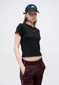 Čierne rebrované tričko s krátkymi rukávmi a malým bielym logom Nike. Kombinované s vínovými saténovými joggingovými nohavicami s bielymi prúžkami.