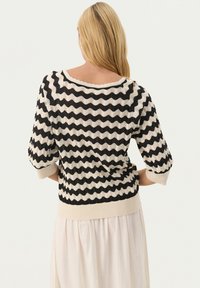 Pull en maille noir et blanc avec un motif en zigzag, manches trois-quarts et design texturé, doté d'un large décolleté et d'une taille côtelée.