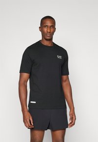 Svart kortärmad träningsskjorta i mjukt tyg, med en liten logotyp på bröstet och meshaccenter på axlarna, matchad med mörka shorts.