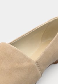 Chaussure plate pour femme en daim beige avec bout fermé et petit talon, présentée en vue rapprochée inclinée.