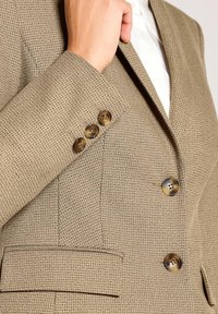Beige blazer met textuur, voorzien van een revers met inkeping, drie bruine knopen aan de manchetten en een nauwsluitend silhouet met een zakdetail.