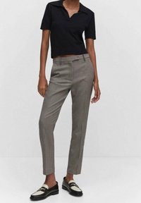 Zwarte cropped poloshirt, grijze geruite op maat gemaakte broek en zwarte loafers met witte accenten. Focus op patronen en een tailored pasvorm.