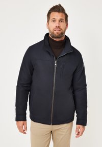 Dunkelblaue isolierte Jacke mit hochgeschlossenem Kragen, Reißverschluss und strukturiertem Material. Verfügt über Seitentaschen und kontrastierende Nähte.
