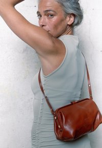 Borsa in pelle marrone con una forma strutturata e una texture liscia. Presenta una lunga tracolla con accessori in ottone e una chiusura superiore.