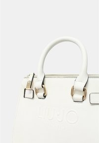 Borsa bianca testurizzata con logo "LIU∙JO MILANO" in rilievo, dettagli in hardware dorato e manici corti e arrotondati. Chiusura con zip nella parte superiore.