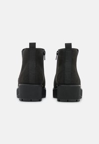 Schwarze Wildleder-Stiefeletten mit Blockabsatz, ausgestattet mit einem schlanken Reißverschluss auf der Rückseite und elastischen Seitenteilen für einfaches An- und Ausziehen. Sichtbare strukturierte Gummisohle.