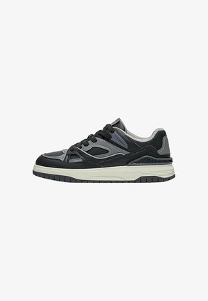 Sneaker basso nero e grigio con suola bianca, lacci neri, tallone in mesh e pannelli superiori sintetici a più strati.