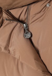 Bruine pufferjackstof met een metallic ritssluiting en een ronde panda-vormige trekker met een gladde, glanzende textuur. Genaaid accent zichtbaar.