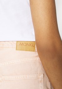 Vaaleanpunaiset farkut, joissa on ruskea nahkainen etiketti, jossa lukee "MONKI" takana. Vaakasuora ompelutyö näkyy taskuissa ja vyötärönauhassa.