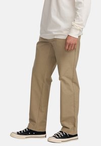 Beige cotton trousers with a straight cut, featuring front pockets and a smooth texture, paired with black canvas sneakers.