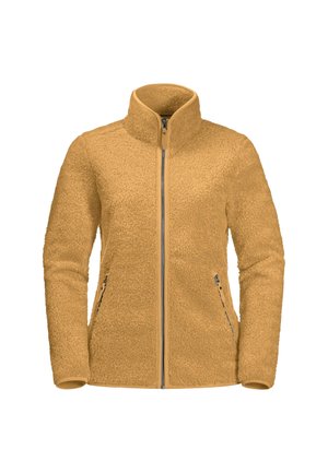 Person trägt eine beige Fleecejacke mit durchgehendem Reißverschluss und hat die Hände in den vorderen Reißverschlusstaschen, kombiniert mit grauer Hose.