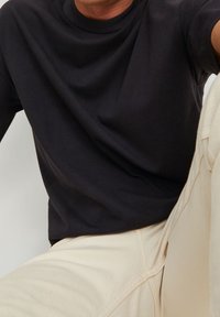 Svart crew-neck sweatshirt med en mjuk textur. Bärs med ljusa beige byxor. Synliga sömmar och avslappnad passform. Minimalistisk design.