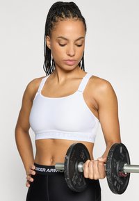 Λευκό αθλητικό σουτιέν με φαρδιές τιράντες και στηρίζον ζωνάρι, σε συνδυασμό με μαύρο κολάν με λογότυπο στη ζώνη. Κρατά βάρος.