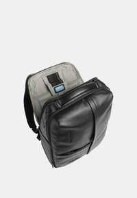 Zaino in pelle nera con una texture liscia. Caratterizzato da una doppia cerniera, tasca frontale e interno grigio con una tracolla e un'etichetta per l'organizzazione.