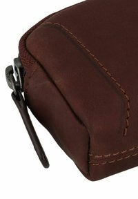 Pochette en cuir marron avec fermeture éclair, présentant des coutures visibles et une texture lisse. Détails incluent une tirette en métal et des bords arrondis.