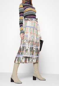 Un pull col roulé rayé multicolore à manches longues associé à une jupe imprimée jusqu'aux genoux et des chaussures à talons carrés beiges.