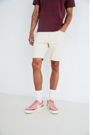 Casual shorts in off-white denim, paired with a maroon t-shirt and pink sneakers. Features include rolled hems and white ankle socks.