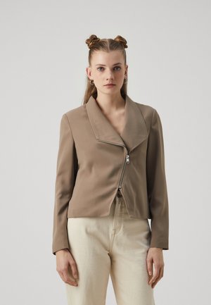 Brown, cropped jacket with a wide collar and a front zipper. Made of smooth fabric, paired with light-colored, straight-leg pants.