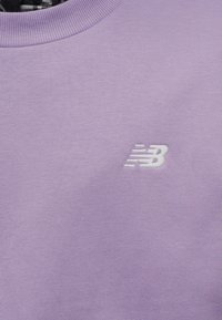 Μωβ φούτερ με στρογγυλή λαιμόκοψη και μικρό λευκό λογότυπο New Balance κεντημένο στο στήθος.