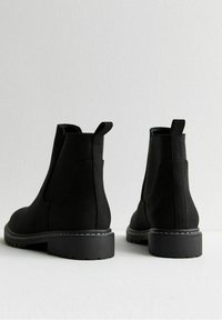Bottes Chelsea en daim noir avec panneaux latéraux élastiques, languettes de tirage et semelle en caoutchouc texturée avec un détail de couture contrastante blanche.